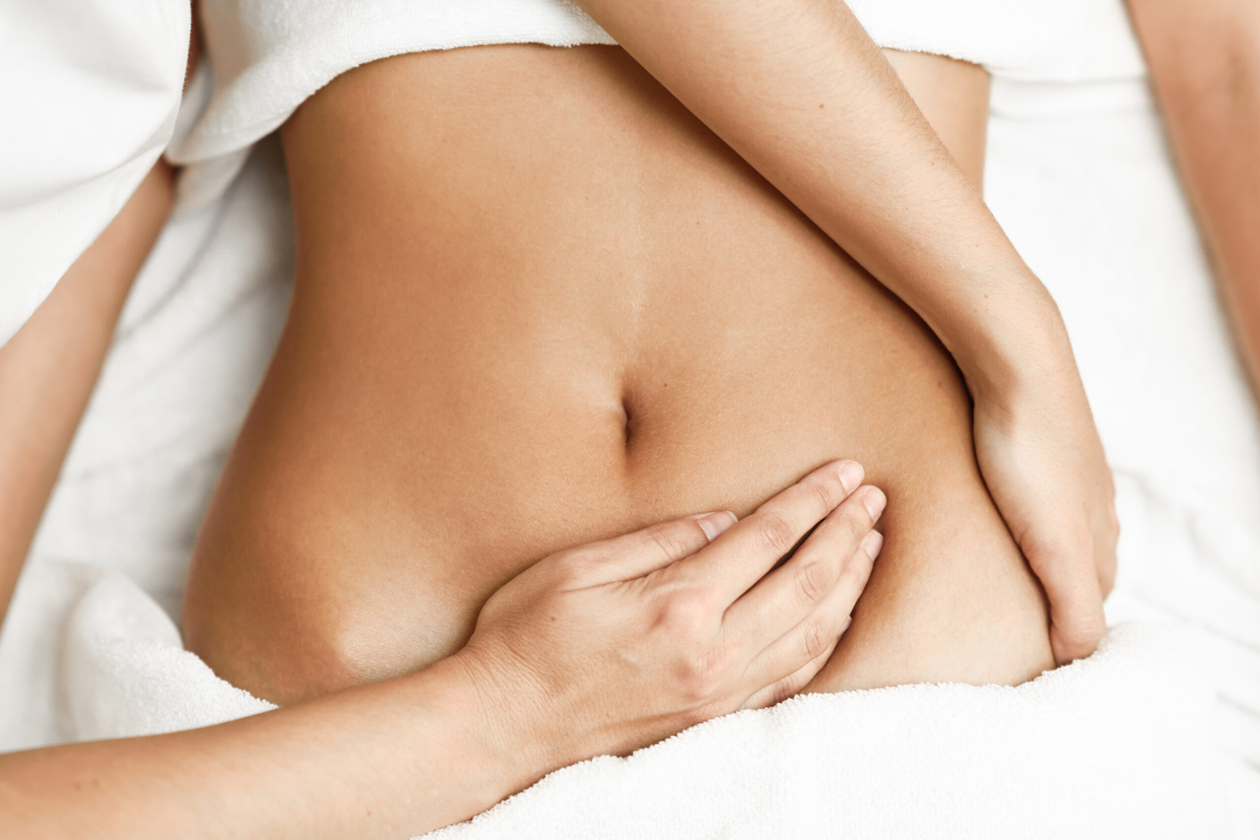 Draufsicht auf Hände, die den Bauch einer Frau massieren. Therapeut übt Druck auf den Bauch aus. Frau erhält Massage in einem Spa-Salon.